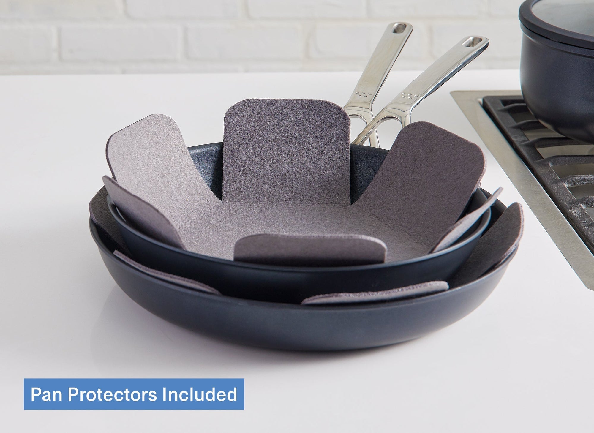 A view of the Misen Pan Protectors nestled between two Misen Nonstick Pans on a white countertop. A caption reads “Pan Protectors Included.”