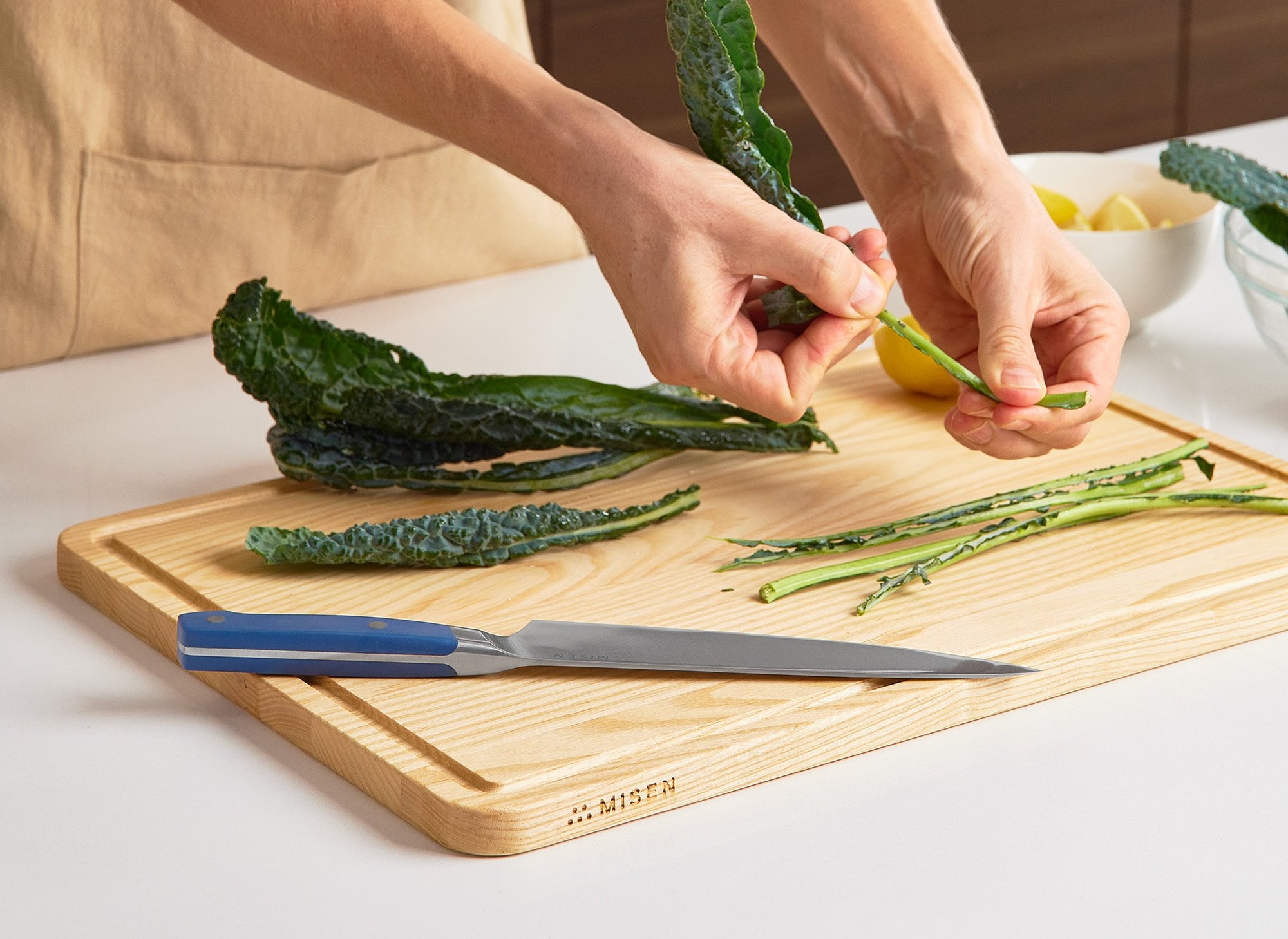 {{large}} A chef de-stems Tuscan Kale atop a Large Misen Wood Cutting Board with a Blue Misen Chef’s Knife visible.