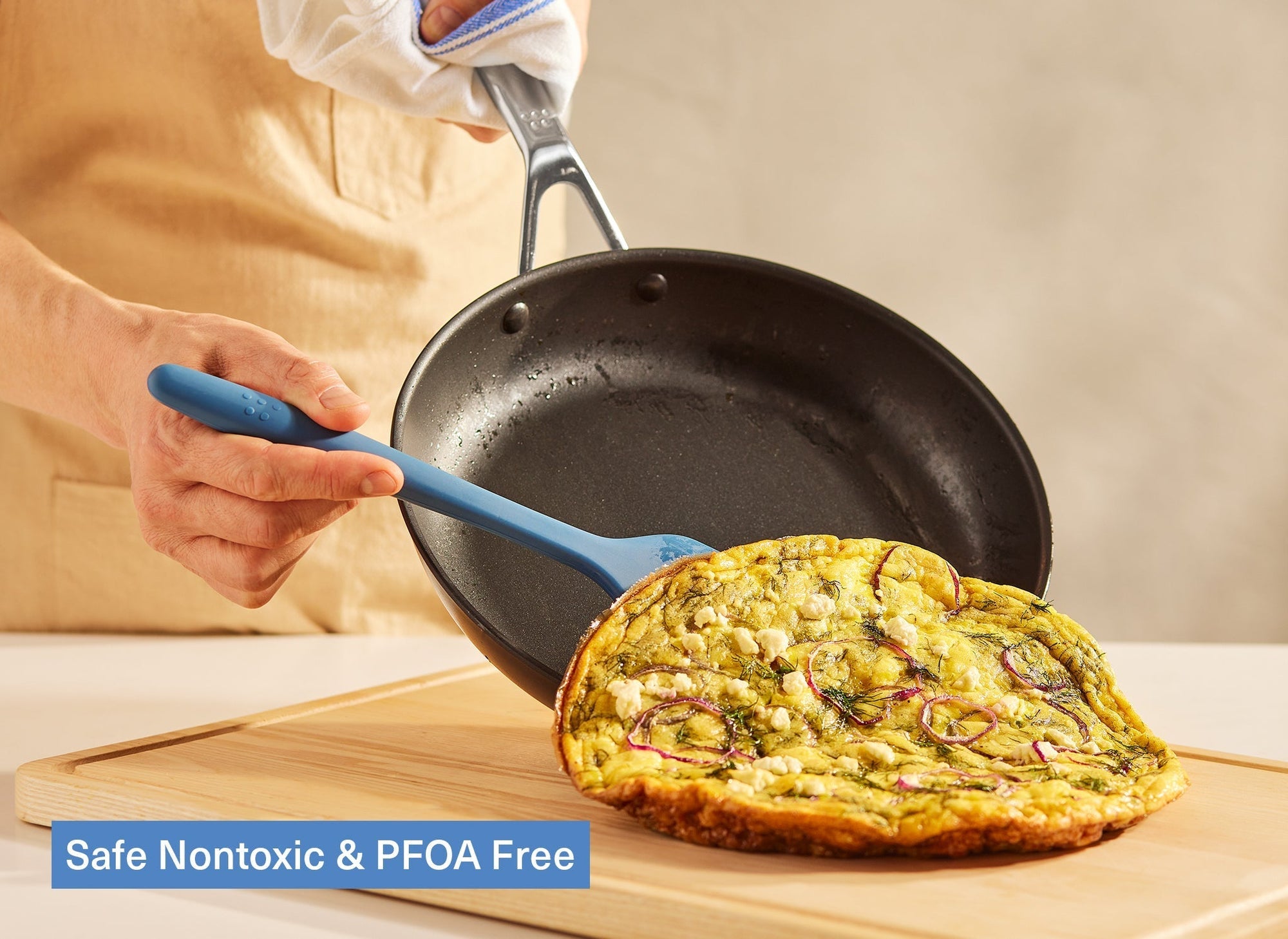 A chef uses a Misen Silicone Spatula to slide a finished frittata out of a Misen Nonstick Pan onto a Misen Wood Cutting Board. A caption reads “ Safe Nontoxic & PFOA Free.”