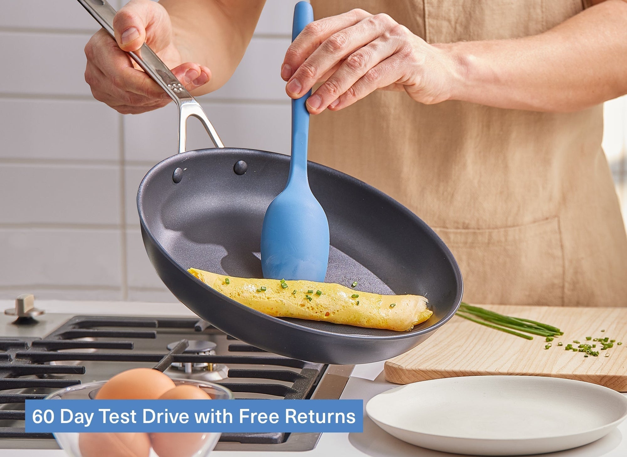 A chef’s hand uses a Misen Silicone Spoontula to fold over an omelet in a Misen Nonstick Pan on a stovetop. A caption reads “60 Day Test Drive with Free Returns.”