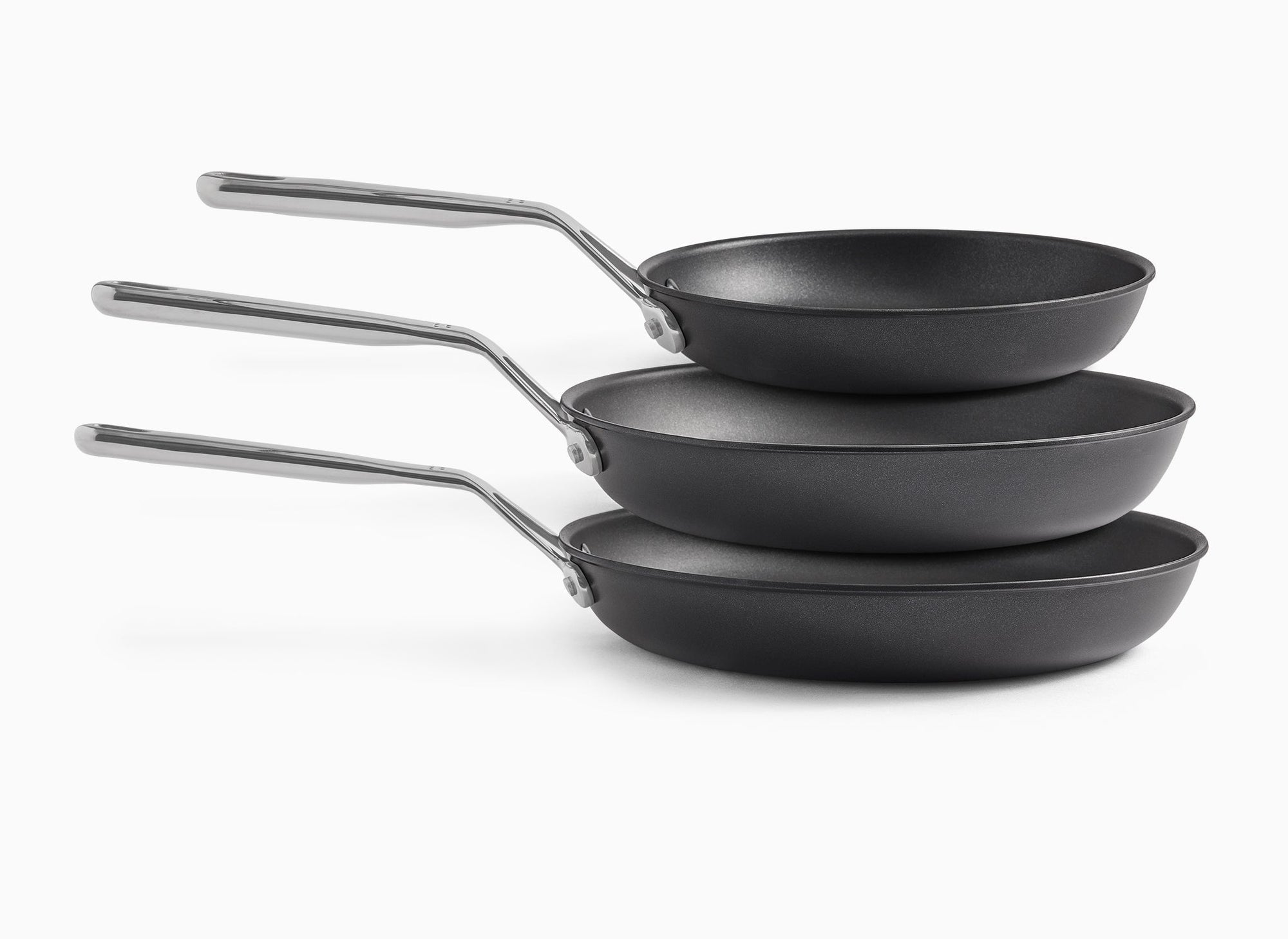 A side view of the 8-inch, 10-inch, and 12-inch Misen Nonstick Pans floating atop each other, about to nestle within each other from smallest to largest, on a white background.
