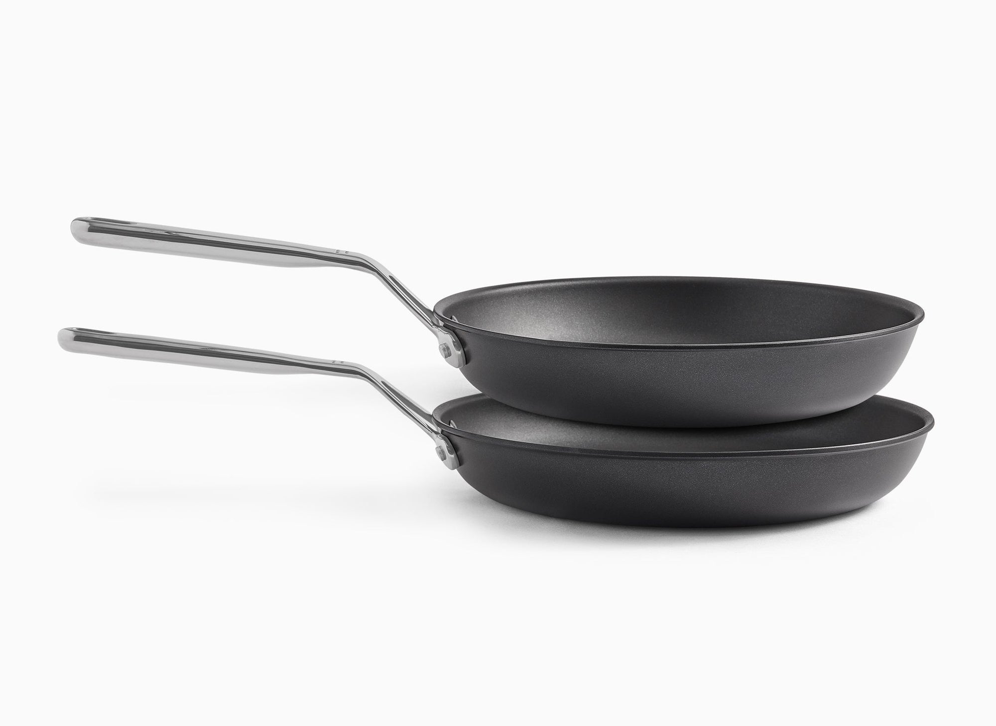 A side view of the 10-inch and 12-inch Misen Nonstick Pans floating atop each other, about to nestle within each other from smallest to largest, on a white background.