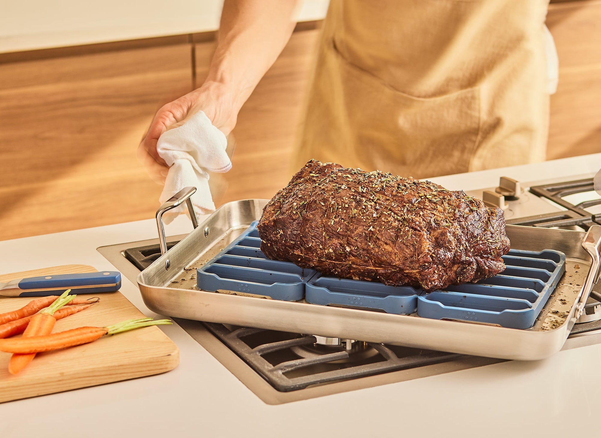 {{oven}} A chef pulls a Misen Roasting Pan out of the oven and sets it on the stovetop. In the Roasting Pan are three blue Misen Silicone Roasting Racks beneath a large roast. 