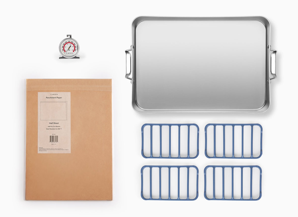 A bird’s eye view of the Misen Oven Bundle on a white background. In the top left, a Misen Oven Thermometer. Top right: the Misen Roasting Pan. Bottom left: a package of Misen Half-Sheet Parchment Paper. Bottom right: four blue Silicone Misen Roasting Racks. 