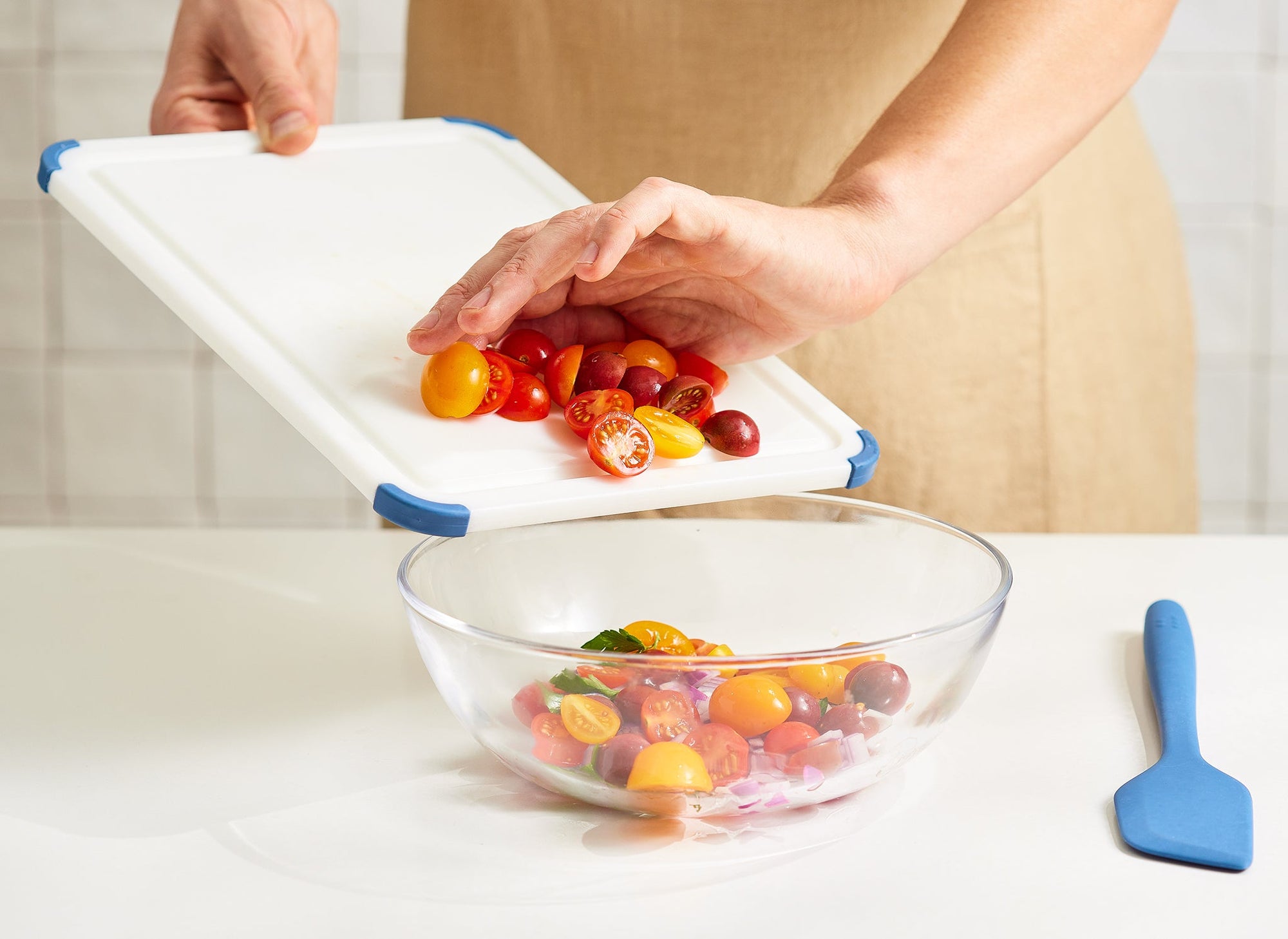 {{small,2-piece-set}} A chef scrapes halved cherry tomatoes off a small Misen Plastic Cutting Board and into a glass bowl.