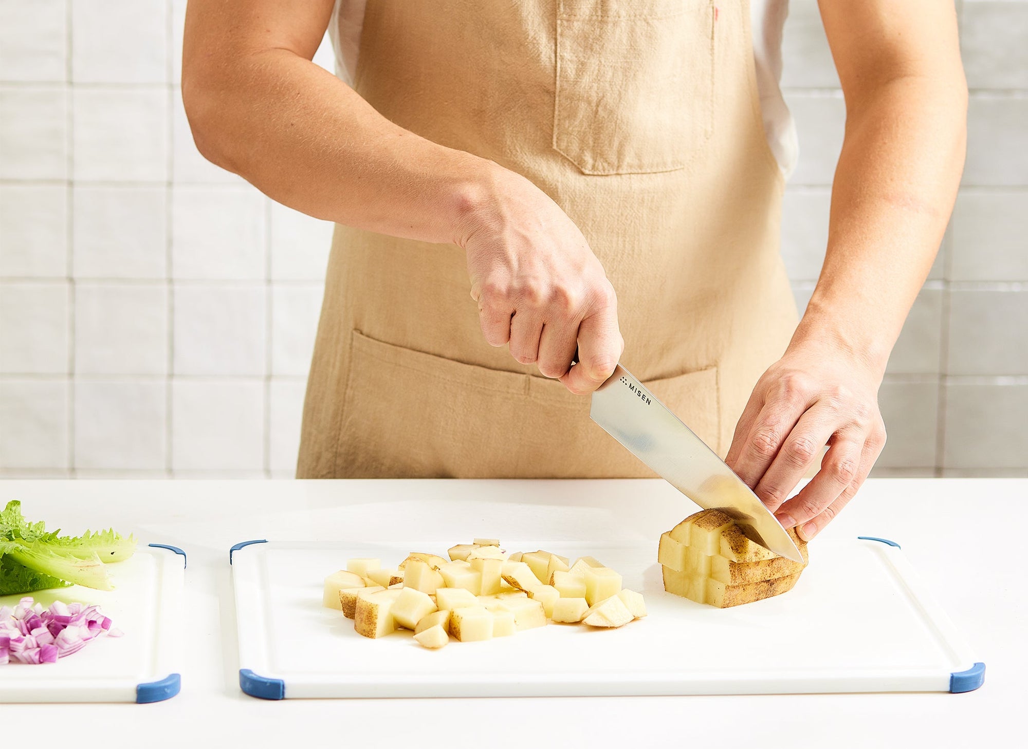 {{large,2-piece-set}} A chef uses a Misen Chef’s Knife to chop potato, red onion, and lettuce on two adjacent Misen Plastic Cutting Boards.