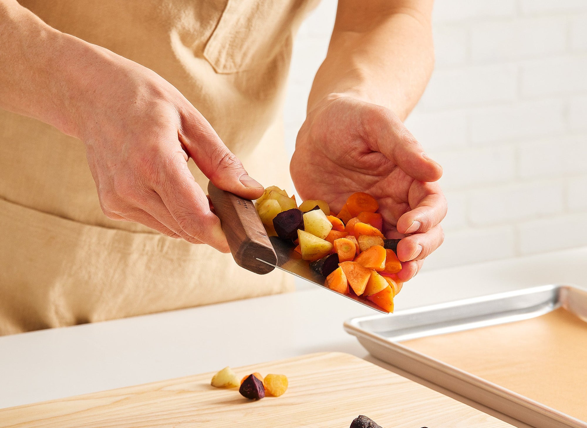 {{walnut,blue}} A pair of hands uses a Misen Bench Scraper with walnut handle to scoop chopped root vegetables up from a Misen Wood Cutting Board.