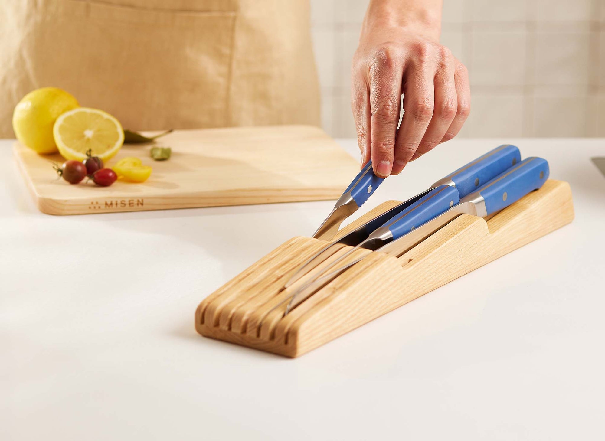 {{ash,walnut}} A chef returns a blue Misen Paring Knife to a full Ash Misen In-Drawer Knife Storage.