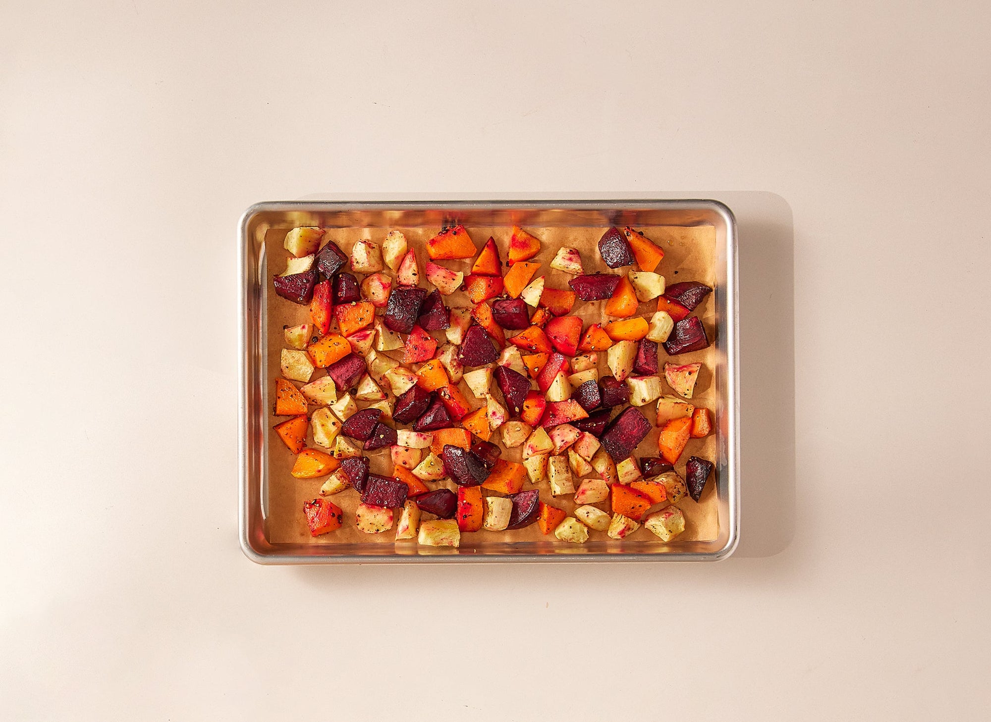 {{half-sheet,quarter-sheet,small-set,large-set}} A bird’s eye view of a Misen Sheet Pan that contains one sheet of Misen Parchment Paper beneath assorted roasted root vegetables such as potatoes and beets. 
