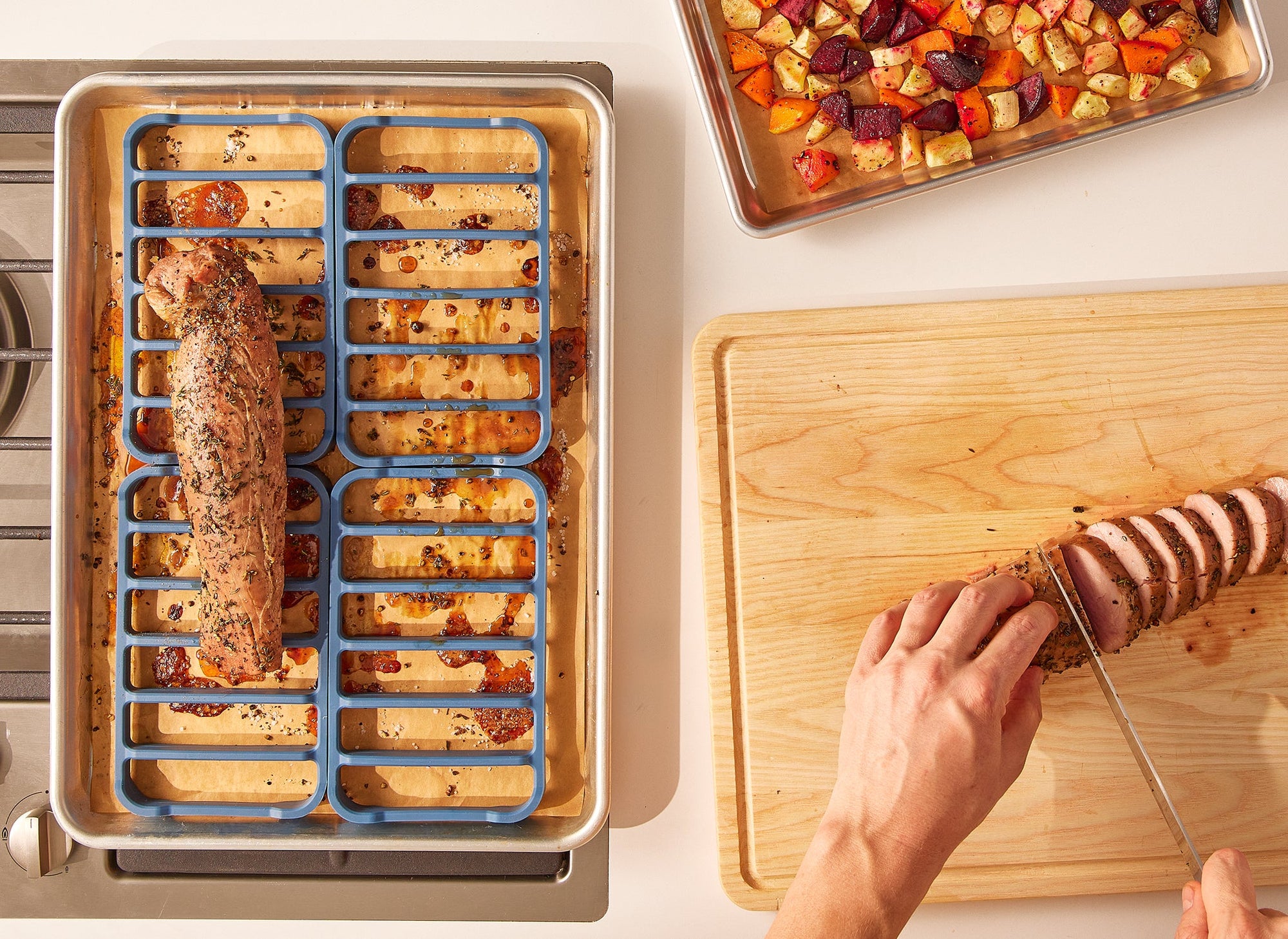 {{4-pack}} A chef slices pork loin on a cutting board. To his left are four Silicone Roasting Racks on a baking sheet, which hold a pork loin. 