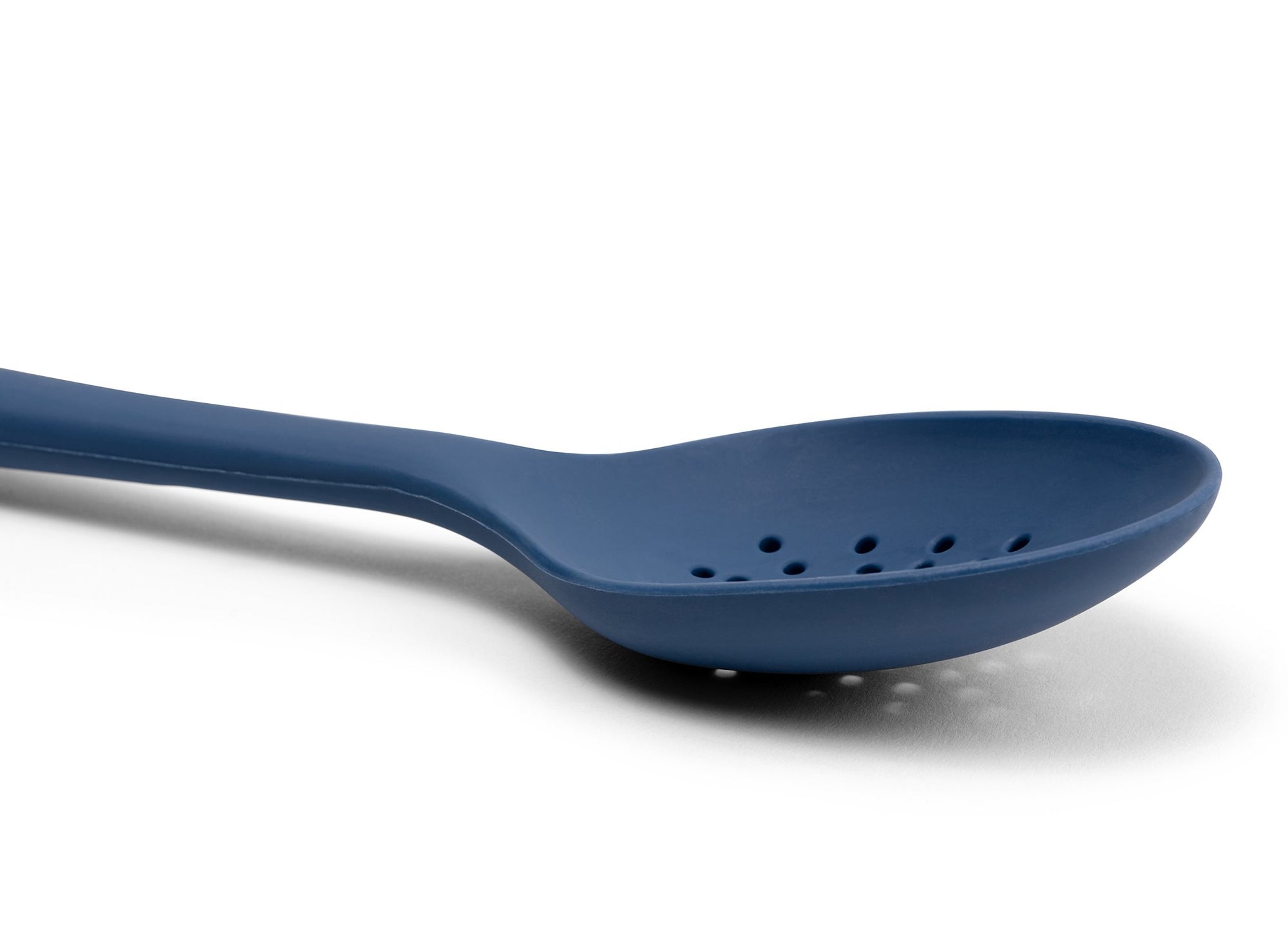 {{blue}} A close view from the side of a Blue Misen Slotted Spoon’s curved head with drainage holes visible on a white background.