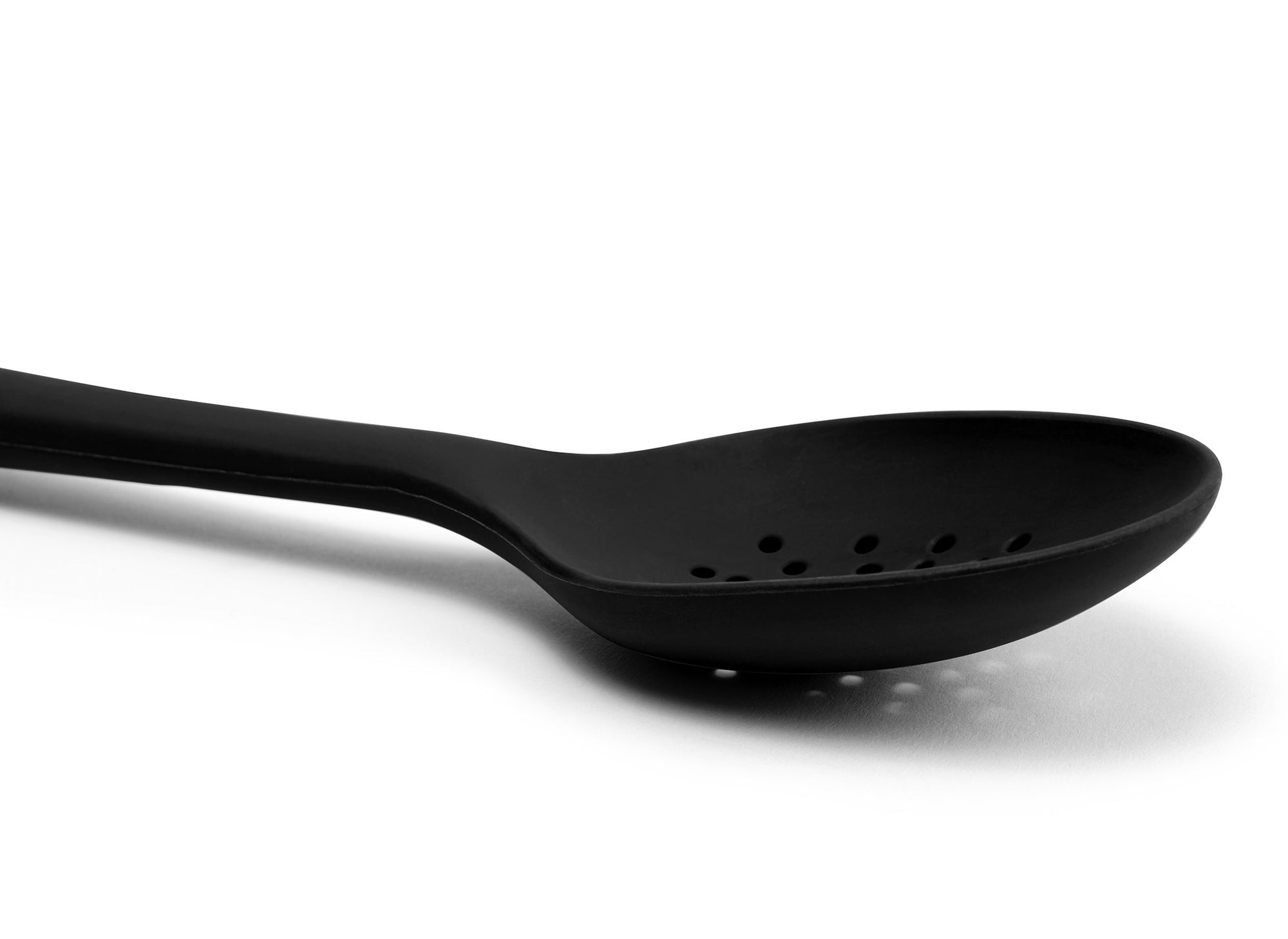 {{black}} A close view from the side of a Black Misen Slotted Spoon’s curved head with drainage holes visible on a white background.