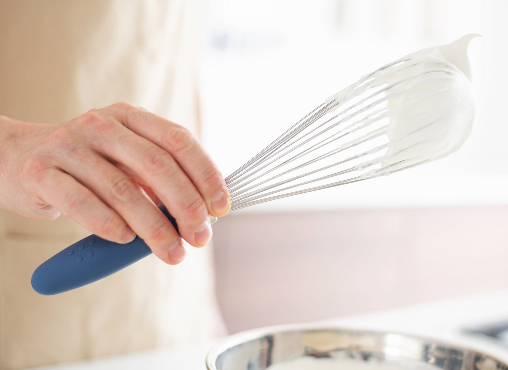 {{blue,black,gray}} Blue Misen Whisk with wire head covered in whipped cream held over a metal mixing bowl on a kitchen countertop.