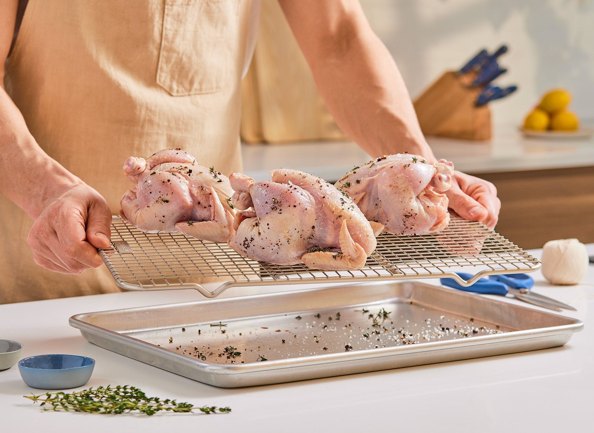 {{quarter-sheet,half-sheet,small-set,large-set}} A chef lifts a Misen Wire Rack out of a Misen Sheet Pan. On the Wire Rack are three small, whole chickens that have been seasoned for cooking.